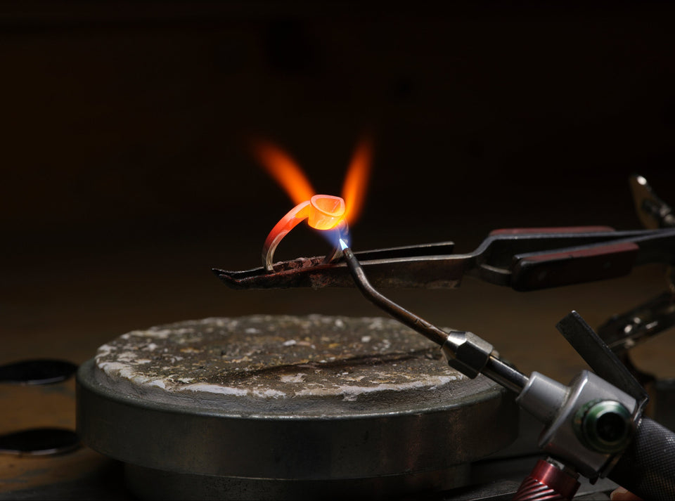 Bespoke jewellery at DMR. Flame from a torch held by tongs on a dark background